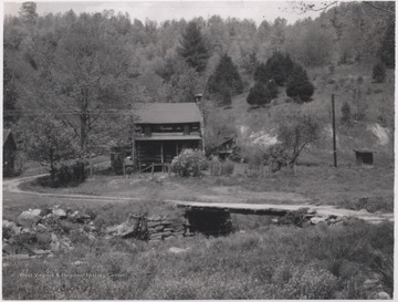 Looking across a dirt road and wooden bridge at a log building. 