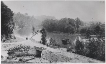 A lone automobile travels on the dirt road that runs alongside the river. The Piers are from a Glen Ray Lumber Company construction site where a railroad bridge is in the process of being built. 