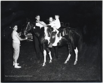 An unidentified man and woman supervise the children sitting on the saddle. 