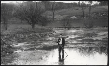 An unidentified man holding a stick stands in a large body of water.