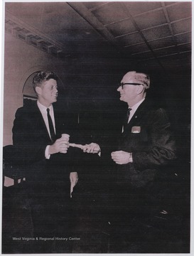 Kee, then administrative assistant of his mother, Congresswoman Elizabeth Kee, hands a light-colored wood gavel to Senator Kennedy who is campaigning for the presidential election against Richard Nixon.