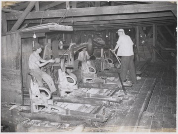Two unidentified employees are pictured inside the company building with sawdust covering the floor. 