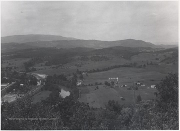 Mountains and hills are pictured in the distance. Small farms scatter across the valley. 