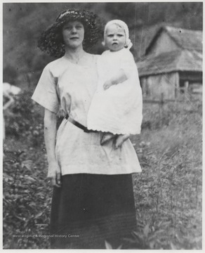 Young holds a child to one side. The two are pictured in a field. 