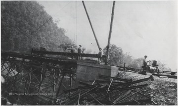 A group of unidentified men stand beside the construction equipment at the site of the bridge to go over the mouth of the Bluestone River. 