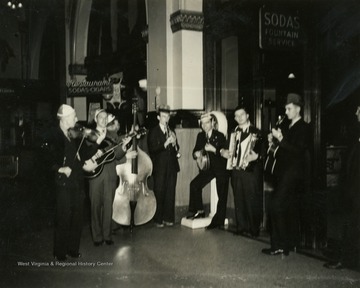 Group is likely the Rhythm Rangers and it appears they are playing inside of a hotel, possibly in Marshall, Missouri during their stay for the National Cornhusking Championship, or somewhere else along the route from Wheeling, West Virginia to the competition. These musicians, like all who worked on the radio broadcast, were employees or immediate family members of the Wheeling Steel Corporation.
