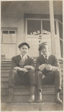 Eldrige Hedrick, left, and Walker boy, right, sit in front of a store advertising "cold drinks, ice cream, candies, and cigars" in its window.