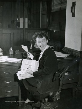 Caption on back of photograph reads: "Part of Regina Colbert's lunch hour is devoted to catching up on correspondence with service men at home and overseas. The "Singing Secretary" writes weekly to a number of men in uniform." Regina Colbert was a performer on the "It's Wheeling Steel" Radio broadcast. This broadcast was ran exclusively by Wheeling Steel Corp. employees and family members, but as the program grew in popularity they began to hire performers with professional backgrounds, like Regina Colbert. However, in order to comply with his rule of an all employee only run program, he would hire these professionals to work in the offices for a period of time. In Colbert's case, she was hired to work as a secretary in the advertising department.