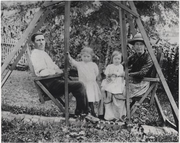 Unknown man and women sit with their daughters on the outdoor furniture. 