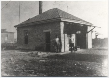 Two unidentified men stand beside the small brick building. 