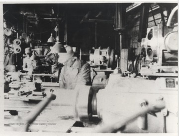 Harold E. Price pictured at lathe in foreground near K. V. Angell, who is pictured in the background to Price's right. 