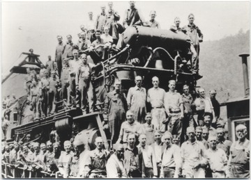 A group of unidentified male employees are pictured around a train outside of the roundhouse building. 