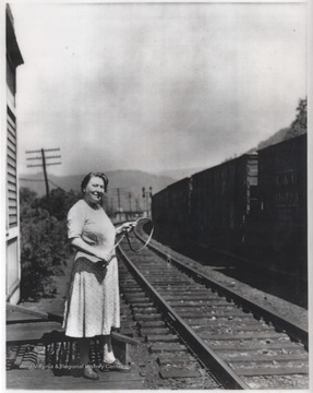 Mrs. E. M. Marable stands outside the cabin beside the railroad tracks. 