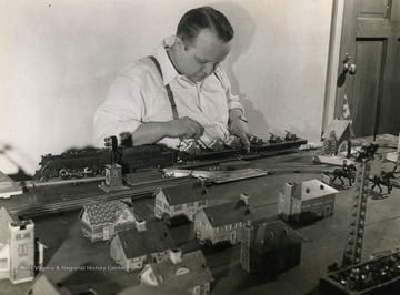 Caption on back of photograph reads: "Bill Griffiths makes military equipment during working hours, relaxes in his spare time by duplicating his day's work in miniature. he built the model guns and tanks shown here, and the train that carries them. On Sundays, he's one of the famed "Singing Millmen"." The Singing Millmen were regulars on the "It's Wheeling Steel" radio broadcast.