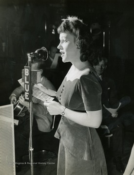 Caption on back of photograph reads: "Regina Colbert is the program's "Singing Secretary", and she lives up to both halves of the title. Featured soloist on Sundays, she is part of the company's secretarial staff weekdays." It was a requirement set by Wheeling Steel Corporation advertising executive John L. Grimes, that the radio broadcast stay an exclusively all employee program. Therefore, Colbert who was not at the time an employee or immediate family member, was hired to work as secretary in the advertising department to maintain this rule.
