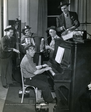 Caption accompanying photograph reads: "Rough and ready war workers on week days, polished network musicians on Sundays are these "Musical Steelmakers", pictured here during an informal rehearsal. They are Russ Anderson at the bass, Tony Biacco with the accordion, Verdi Howells the goggled sax man, Jimmy Snodgrass on the drums, and Dayton Powell at the piano."