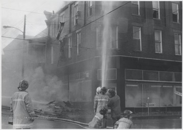 A group of unidentified firemen fight the fire inside a three story brick building originally housing Rose's Drug Store, Co. 