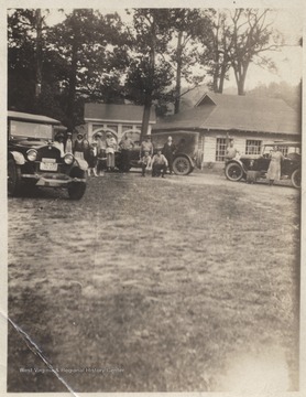 A group of unidentified people are pictured beside their parked automobiles outside the building where a spring runs through the outdoor deck.