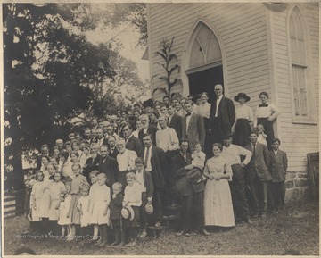 Frank Kesler pictured in a dark suit standing in the back row, on the right between a group of ladies. Other subjects unidentified.