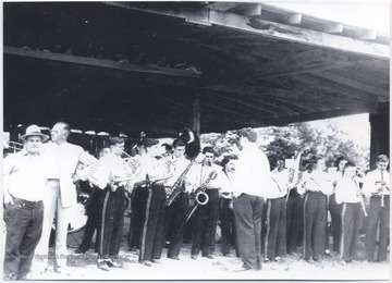 High school musicians pictured with their instruments rehearsing under a pavilion. Subjects unidentified. 