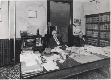 Ball (left) and Daly (right) sit behind a desk in what appears to be Ball's office.