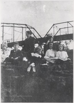 Two women and a group of children are pictured on top of rocks beneath the toll bridge. 