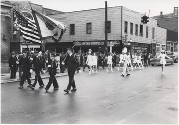 Uniformed soldiers, holding the American and West Virginian flags, are trailed by marching band members make their way through the streets of Hinton as spectators look on from the sidewalks. 