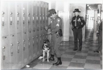 Law enforcement officials stand by while a dog is led down the hallway in search of drugs.