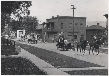 Two men on horses lead automobiles and parade floats down Temple Street. 