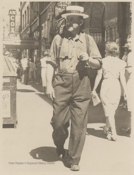 An unidentified man walks in the foreground of the photo while behind him people exit and enter the A. W. Cox store.
