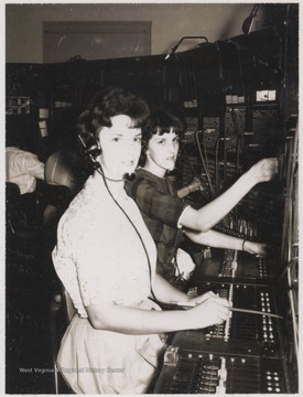 Two unidentified women sit behind the switchboard at the telephone exchange. 