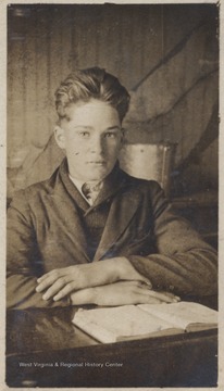Portrait of the boy behind a desk with a book. Walker and his family were displaced by the Bluestone Reservoir Project. 