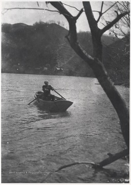 An unidentified man pulls the boat's oars across the water. 