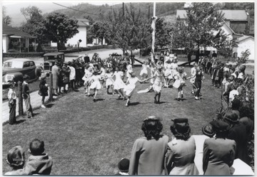 Young girls run around the maypole decorated in streamers. Subjects unidentified. 