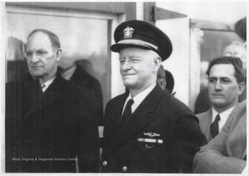 Behind Nimitz is R. C. "Cleve" Hayner (left) and E. L. Hellem (right). Nimitz is pictured in his Naval uniform.