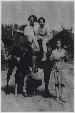 Minnie, pictured in a tie, sits on a horse beside an unidentified girl. 