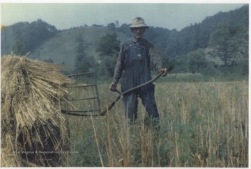 Shumate holds a farming tool while posing beside a stack of hay. The farm is located near War Ridge.