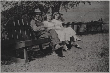 Luther, Glenna, and Gladys Shumate sit on a bench outside of their home.