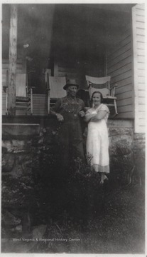 Uncle Charley and Aunt Eva pictured in front of the home's porch where three rocking chairs sit idly. 