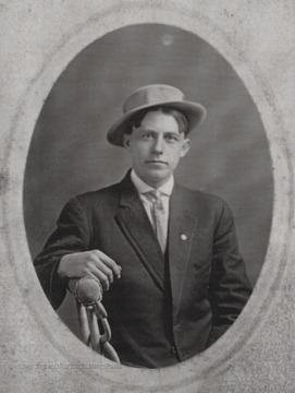 Oran, brother to H. D. Thompson, is pictured sitting on a chair in a suit and hat at an unkown location.