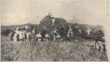 A group stands around a large haystack while some take it upon themselves to climb it. Subjects unidentified.