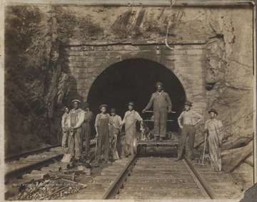 The foreman stratling the rail is C. E. Long. Track workers Jim Adams is at the far left. "M. J." is inscribed on the photograph above the cluster of workers. The rest of the men pictured are unidentified.