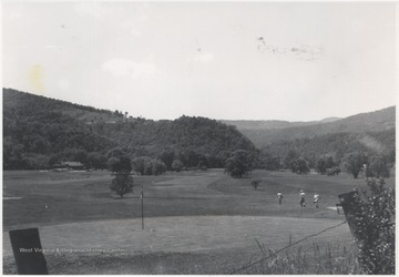 Three men walk across a lawn with their golf gear. The country club house sits on the left. Subjects unidentified.