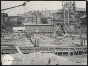 An unidentified man stands in the middle of the construction site looking around at the progress. In the background is Stalnakar Hall. 
