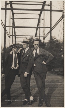 Three unidentified men put their arms around each others shoulders while posing on the bridge.