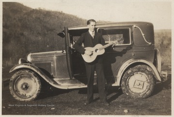 The unidentified family member stands in front of a muddy automobile while strumming the instrument. 