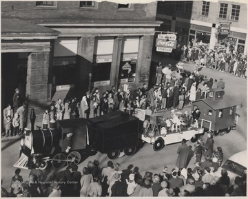 A crowd watches at the intersection of 2nd Avenue and Ballengee Street as a parade float disguised as a train drives by.