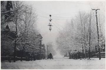 A man makes his way down the snowy street with his horse-drawn wagon. 