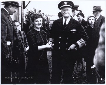To the far left is Senator Jennings Randolph with an unknown child.  Bonnie Peck, a WVU Extegent Agent, shakes hands with Admiral Nimitz. In the background, Lucille Hinton and her husband, Howard Hinton, are pictured. 