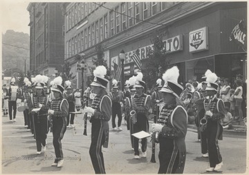 The band moves along the corner of 2nd Avenue and Temple Street while spectators watch from the sidewalks. Subjects unidentified.